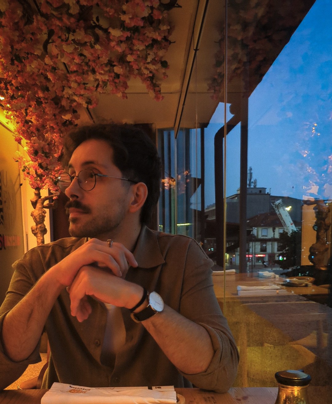 A person is sitting at a table with a window overseeing the neighbouring houses to the right.