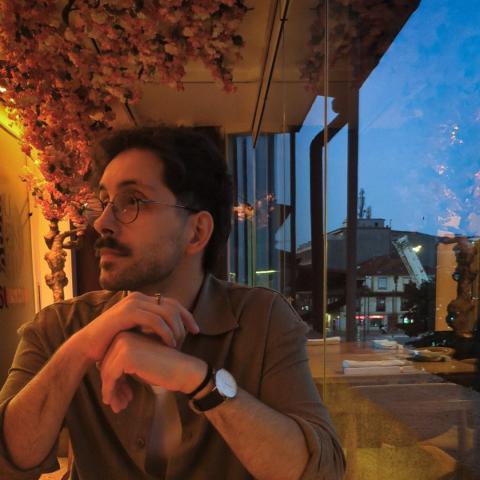 A person is sitting at a table with a window overseeing the neighbouring houses to the right.
